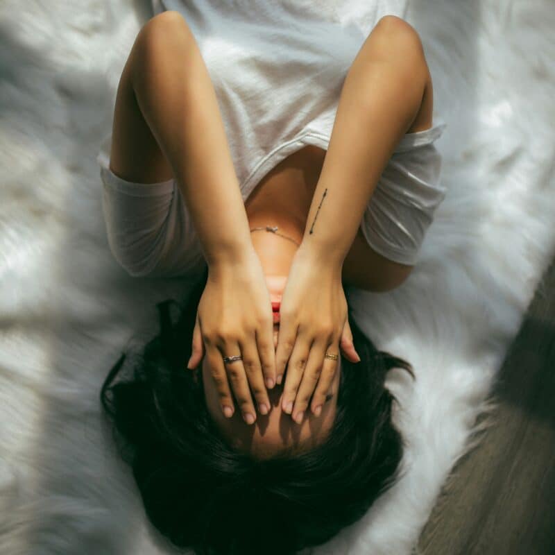 Woman lying on a soft rug with hands over her face, illustrating the potential relief CBD oil offers for endometriosis-related pain and stress.