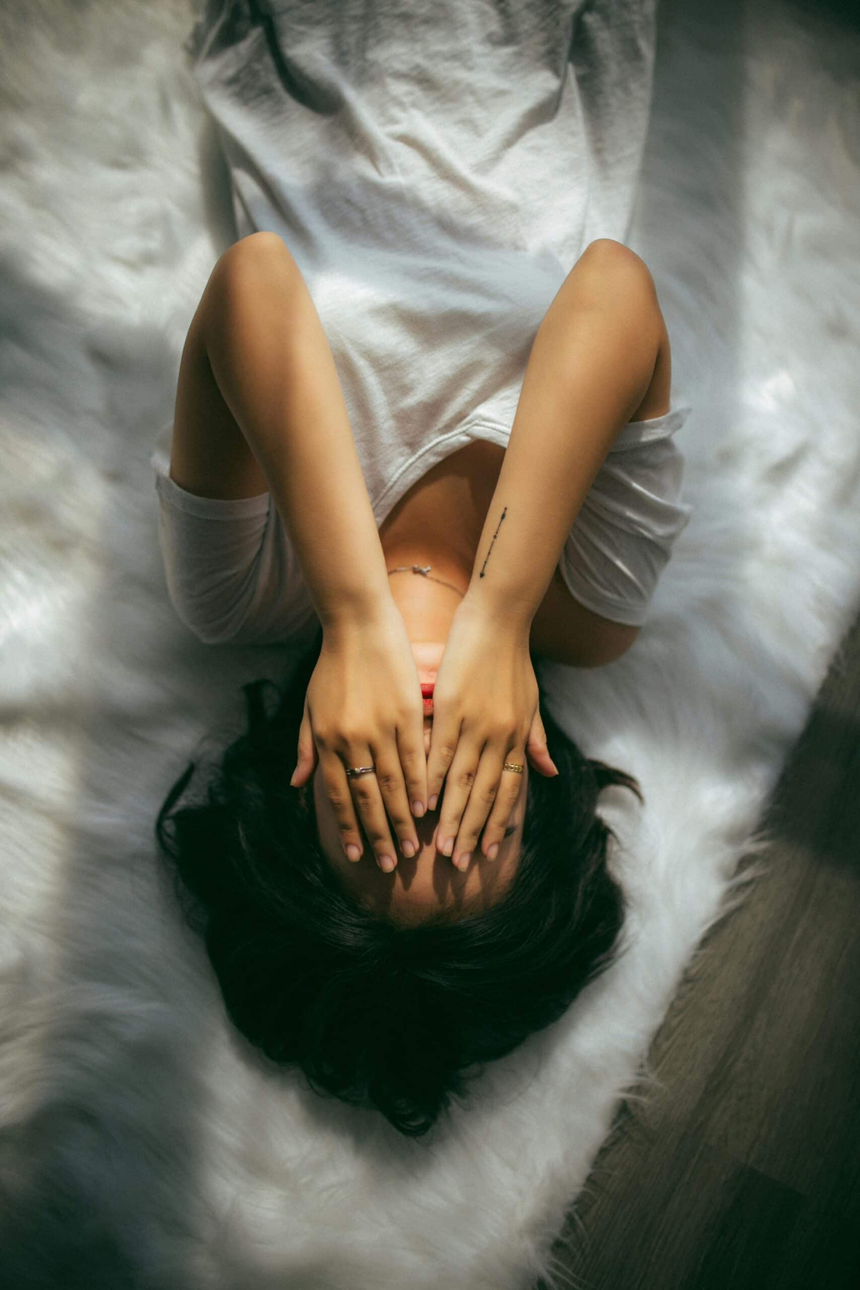 Woman lying on a soft rug with hands over her face, illustrating the potential relief CBD oil offers for endometriosis-related pain and stress.