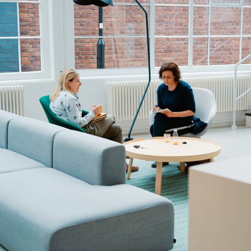 Two women engaged in a supportive conversation in a bright, welcoming space, reflecting efforts to improve quality of life through connection.