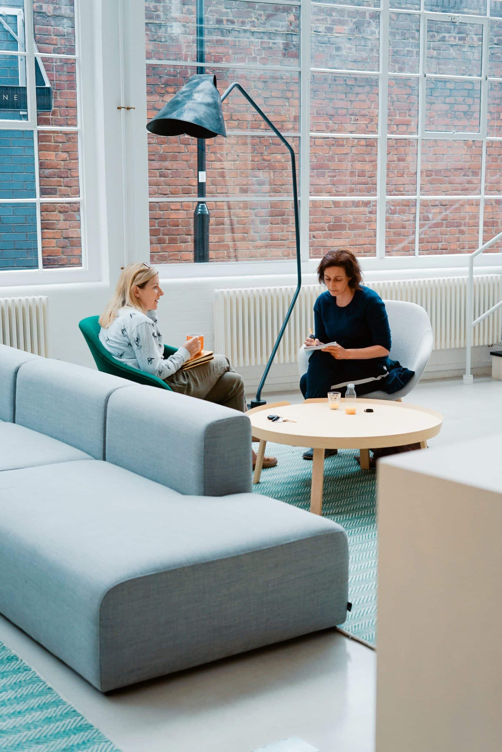 Two women sitting at a table, discussing in a bright and open space. One of them is listening attentively to the other, symbolizing a collaborative discussion about healthcare advocacy for endometriosis treatment coverage.