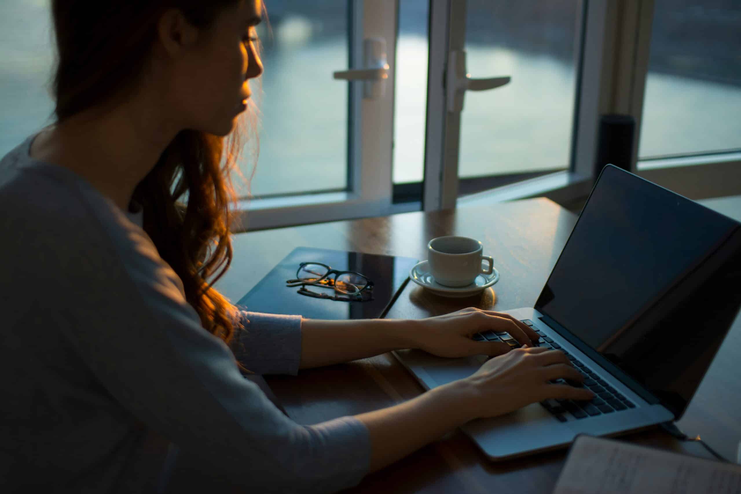 A woman working on her laptop in a cozy, sunlit room, reflecting a moment of focus, potentially related to organizing marketing crowdfunding efforts for endometriosis care.