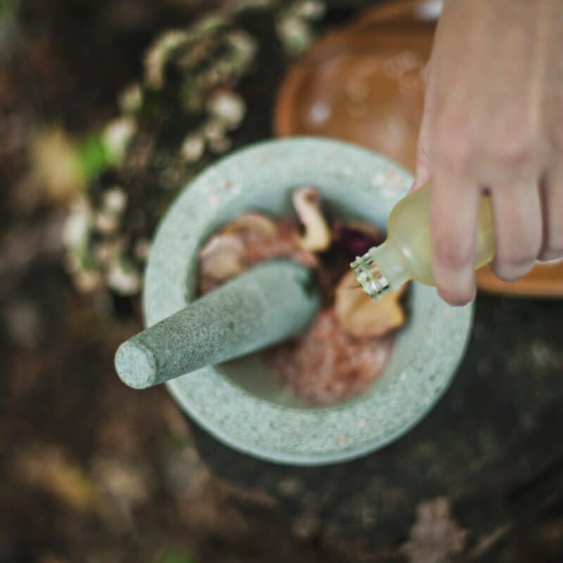 A hand pouring herbal oil into a mortar and pestle with natural ingredients, symbolizing the fusion of traditional and alternative approaches in endometriosis care for holistic healing.