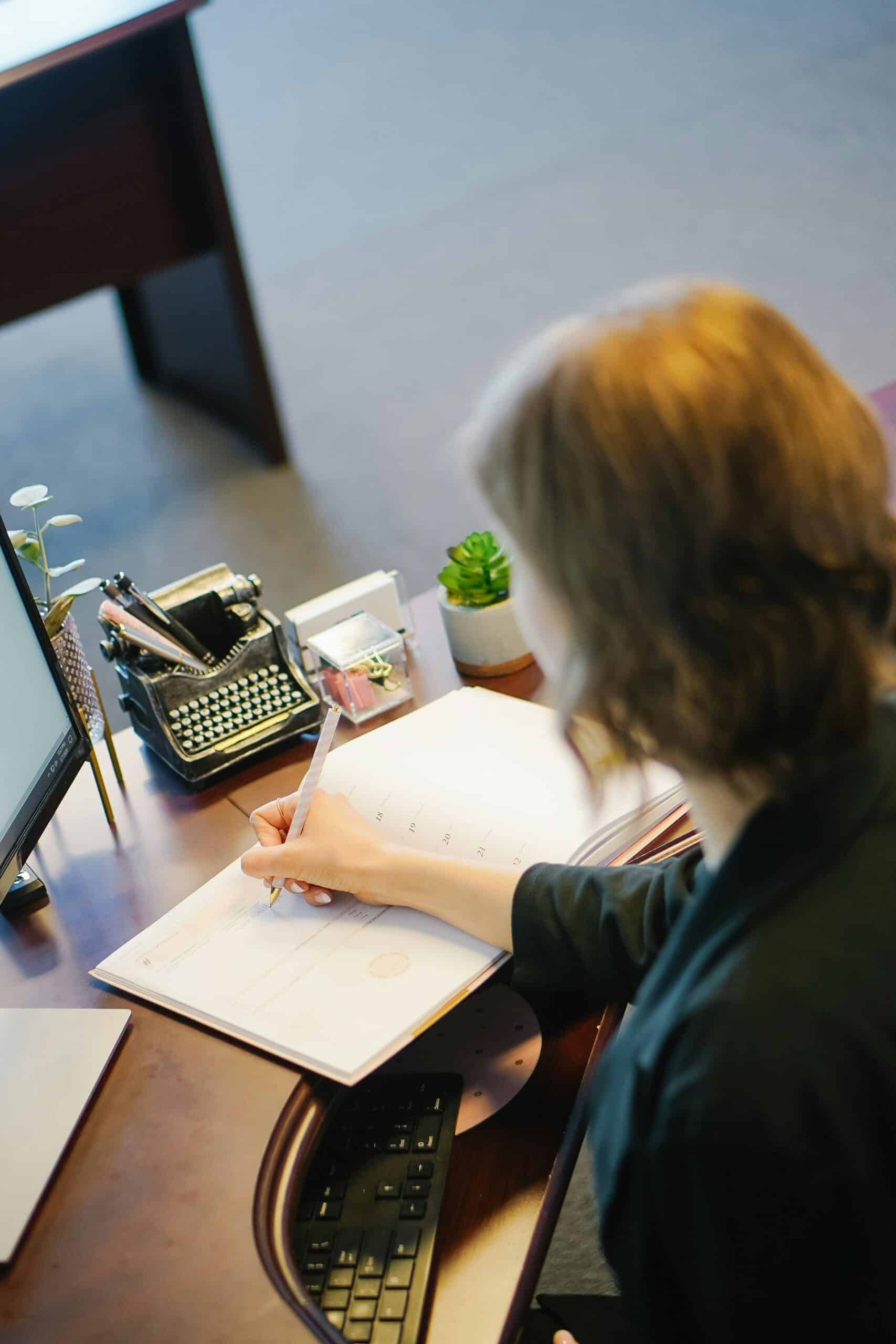 A person writing in a planner while working at a desk, symbolizing the process of organizing tasks such as researching financial aid resources for endometriosis patients.