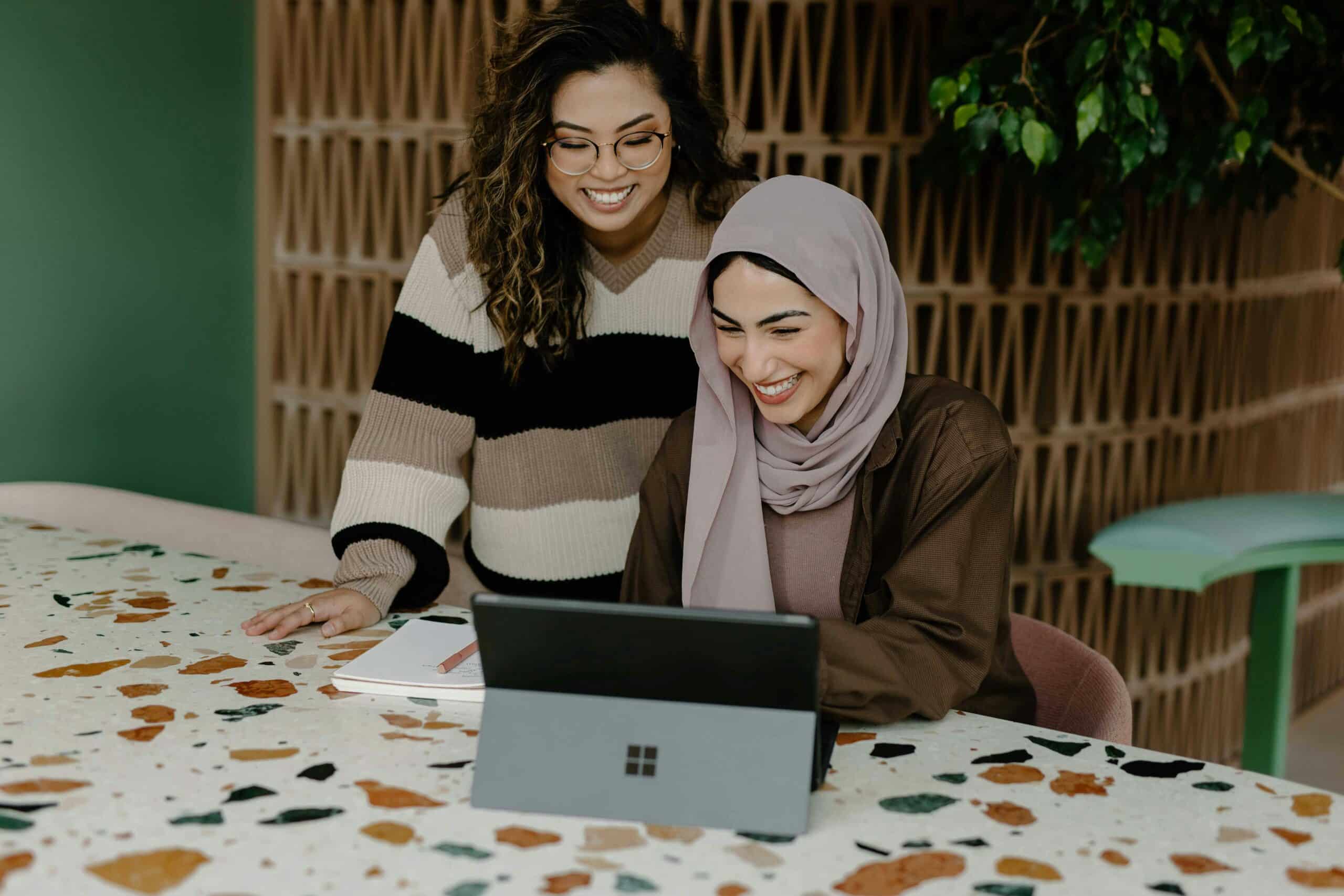 Two women smiling and working together on a tablet, likely collaborating on a marketing project for crowdfunding for endometriosis care.