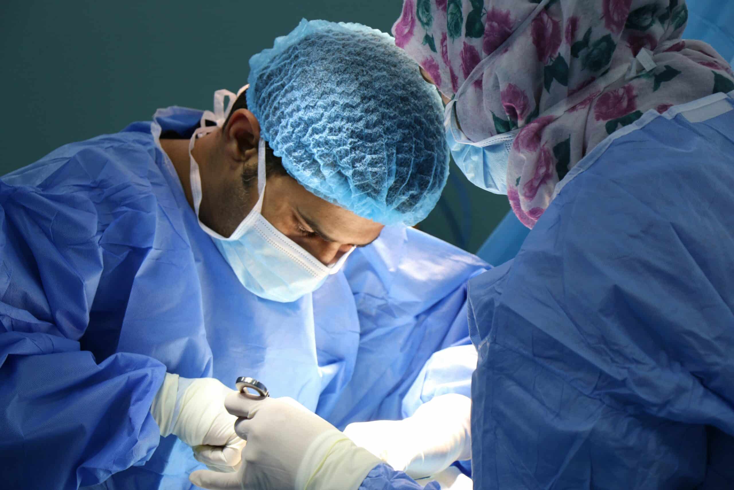 Surgeons in blue surgical gowns and protective gear performing a procedure with precision, representing an overview of endometriosis excision surgery. - Rachael Haverland Site Surgeons in blue surgical gowns and protective gear performing a procedure with precision, representing an overview of endometriosis excision surgery.