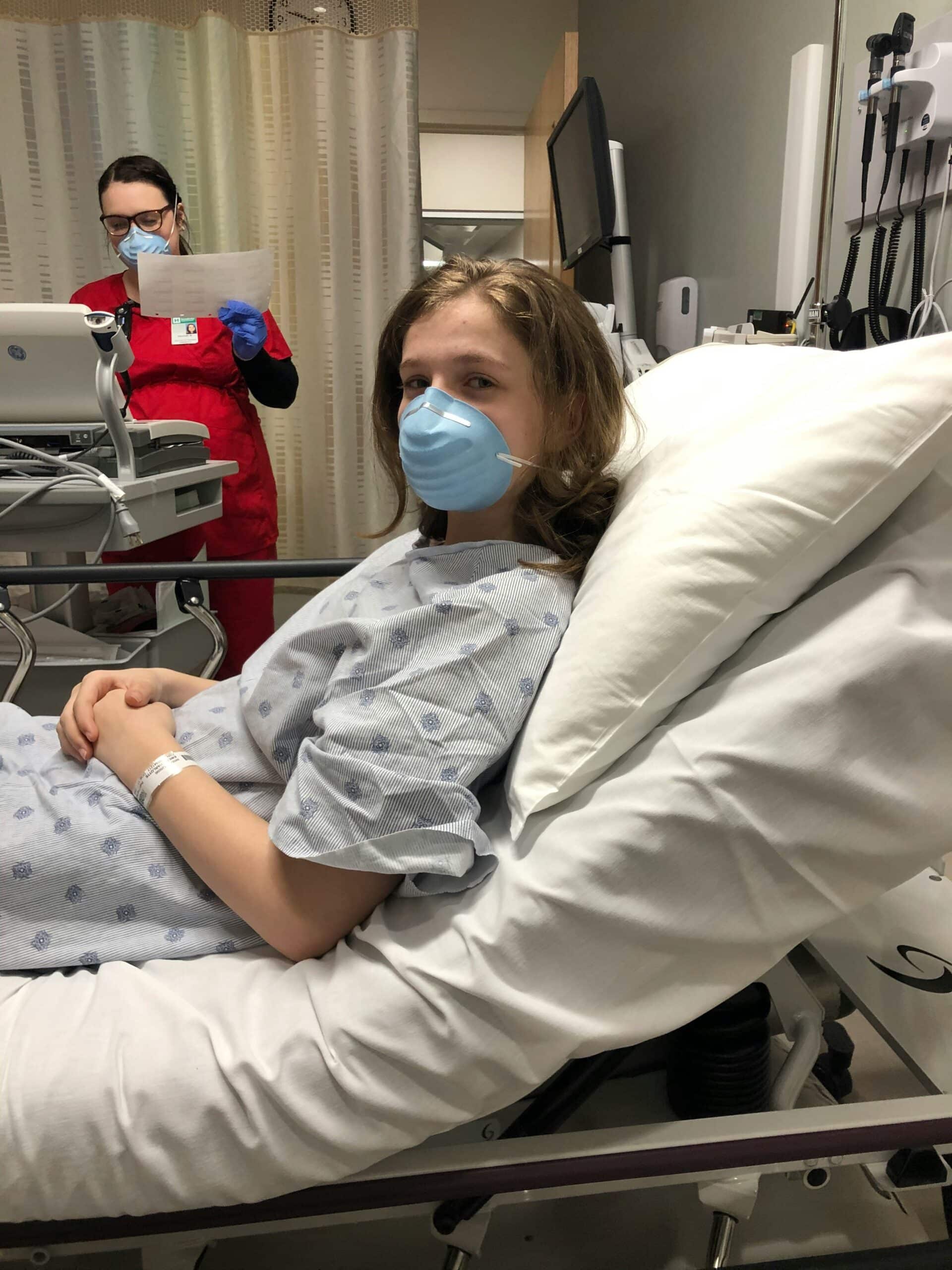 A patient lying in a hospital bed wearing a medical mask, with a healthcare professional reviewing documents in the background, representing the challenges of understanding endometriosis and its symptoms.