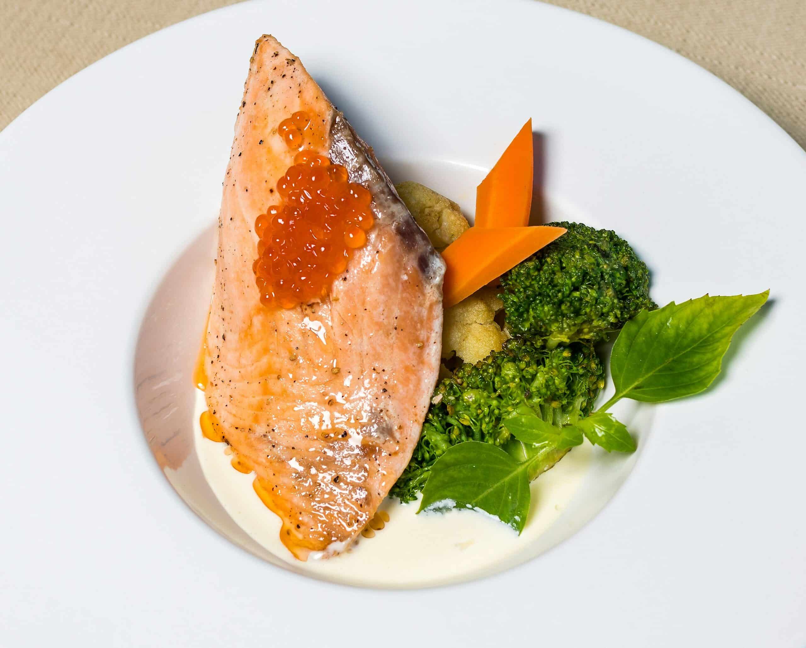 A plated salmon dish topped with fish roe, accompanied by broccoli, carrots, and fresh basil, highlighting the potential of omega-3 fatty acids in alleviating endometriosis symptoms through diet.