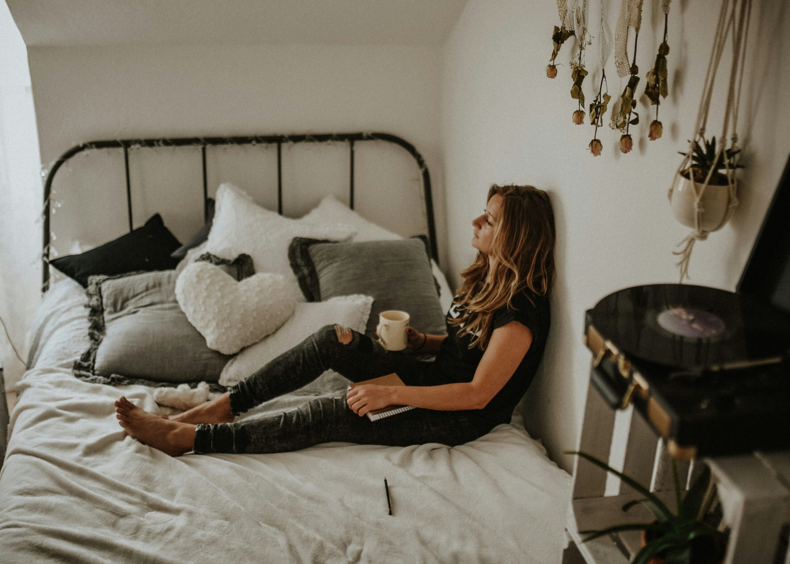 A woman sits quietly on her bed holding a mug, appearing deep in thought, highlighting the challenge of distinguishing endometriosis pain from anxiety-related physical symptoms. - Rachael Haverland Site A woman sits quietly on her bed holding a mug, appearing deep in thought, highlighting the challenge of distinguishing endometriosis pain from anxiety-related physical symptoms.