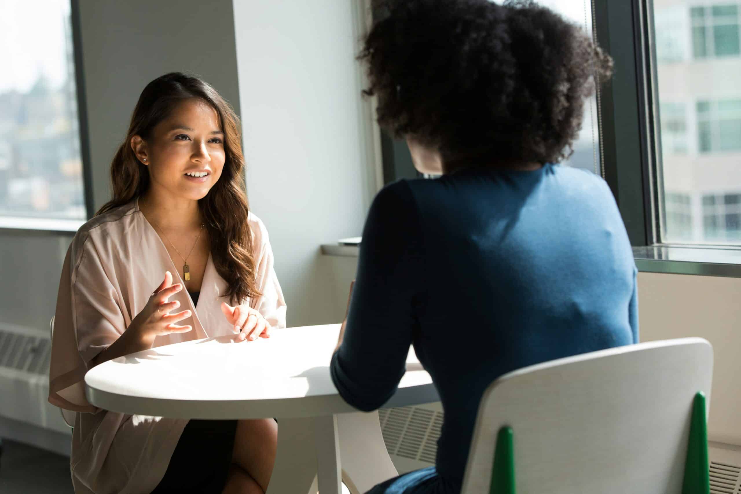 two women talking at a table in a workplace setting - Rachael Haverland Site two women talking at a table in a workplace setting
