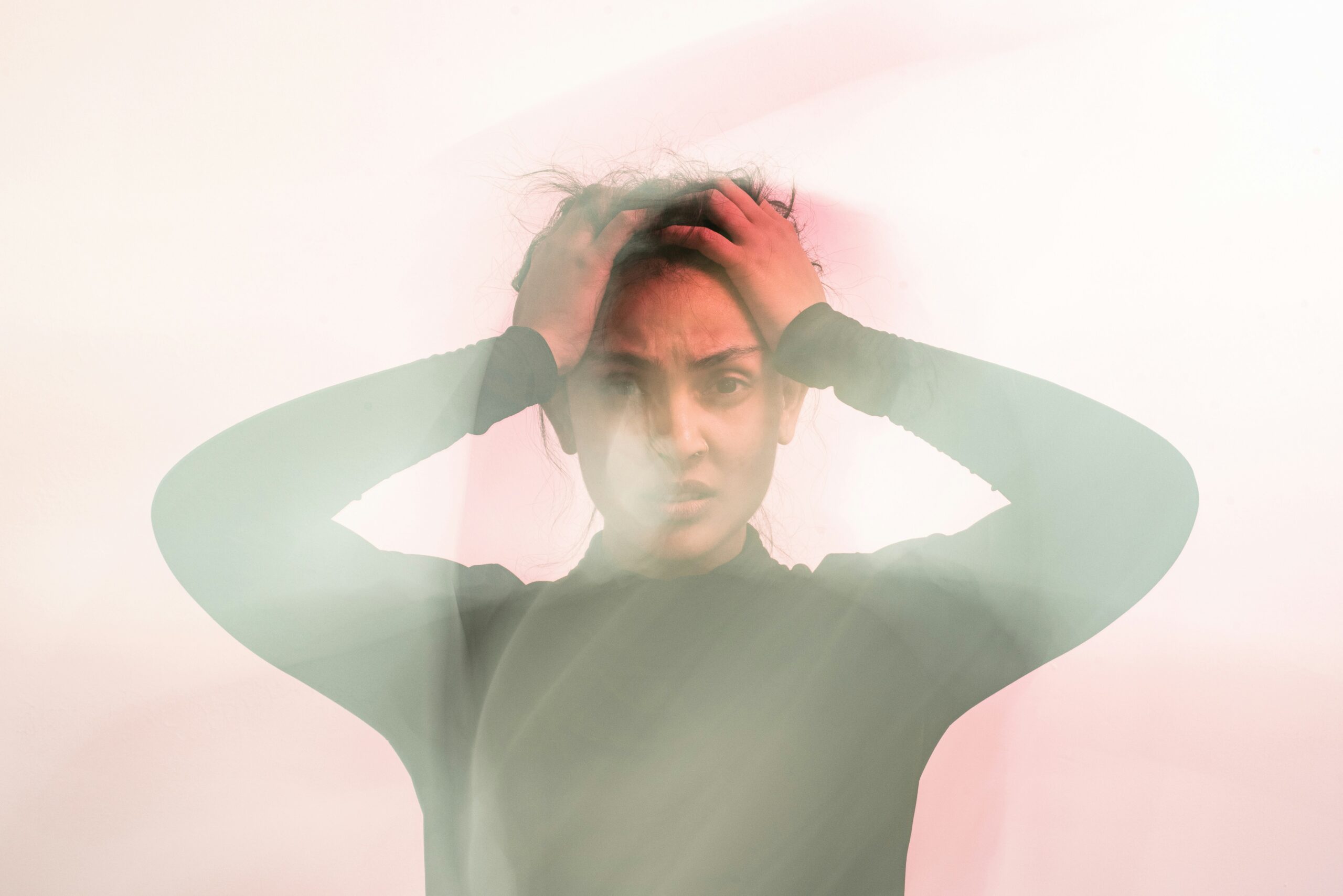 A woman holds her head in distress with blurred motion around her, symbolizing the confusion and tension that often mask subtle signs of anxiety in endometriosis. - Rachael Haverland Site A woman holds her head in distress with blurred motion around her, symbolizing the confusion and tension that often mask subtle signs of anxiety in endometriosis.