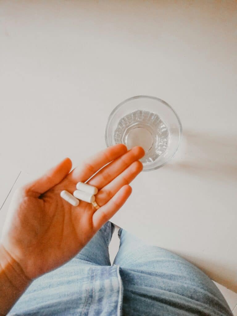 girl holding supplements with a glass of water nearby