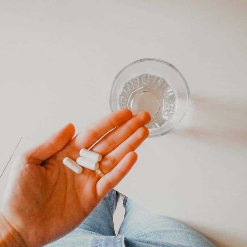 girl holding supplements with a glass of water nearby