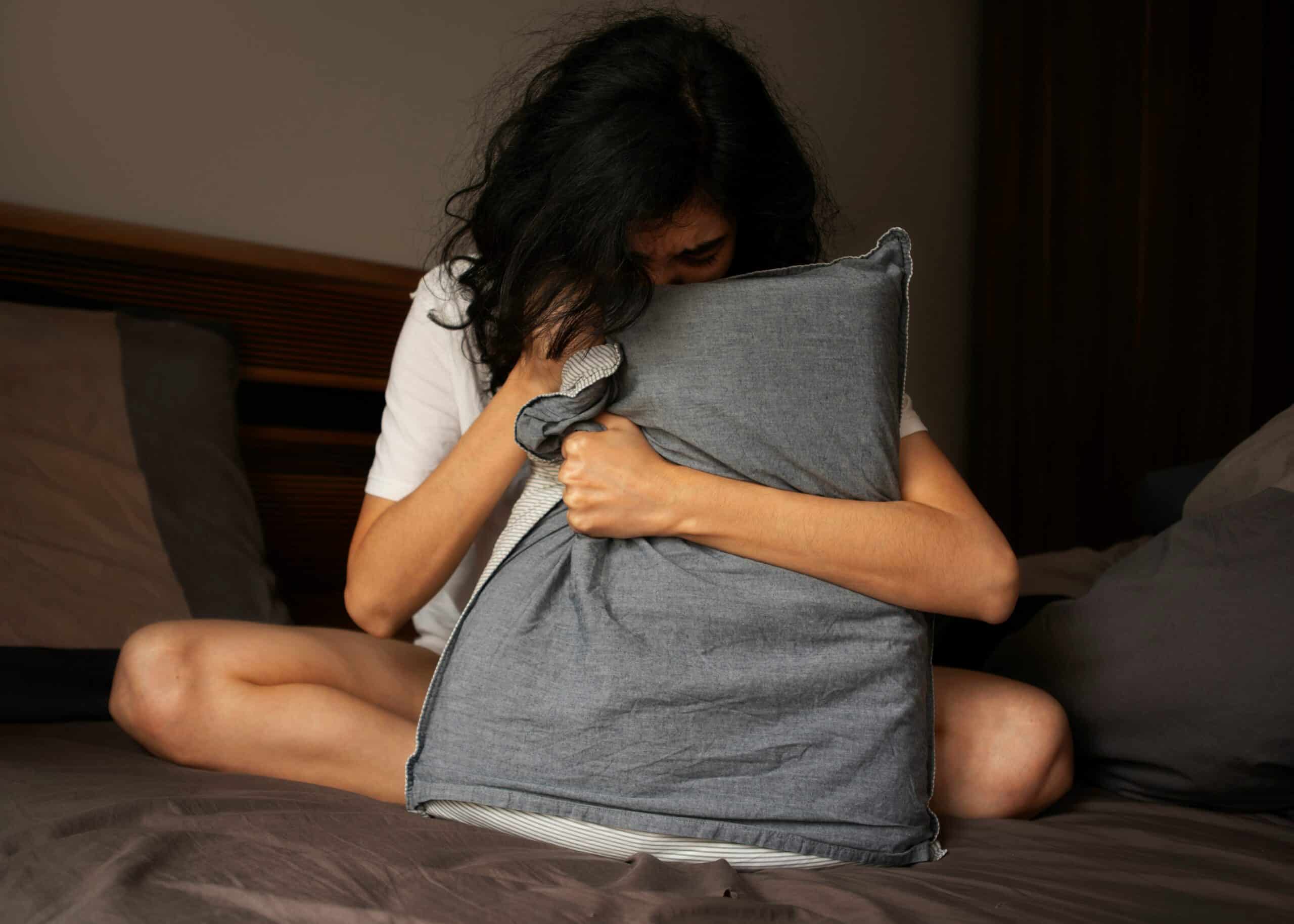 Woman sitting on bed, hugging pillow in pain. - Rachael Haverland Site Woman sitting on bed, hugging pillow in pain.