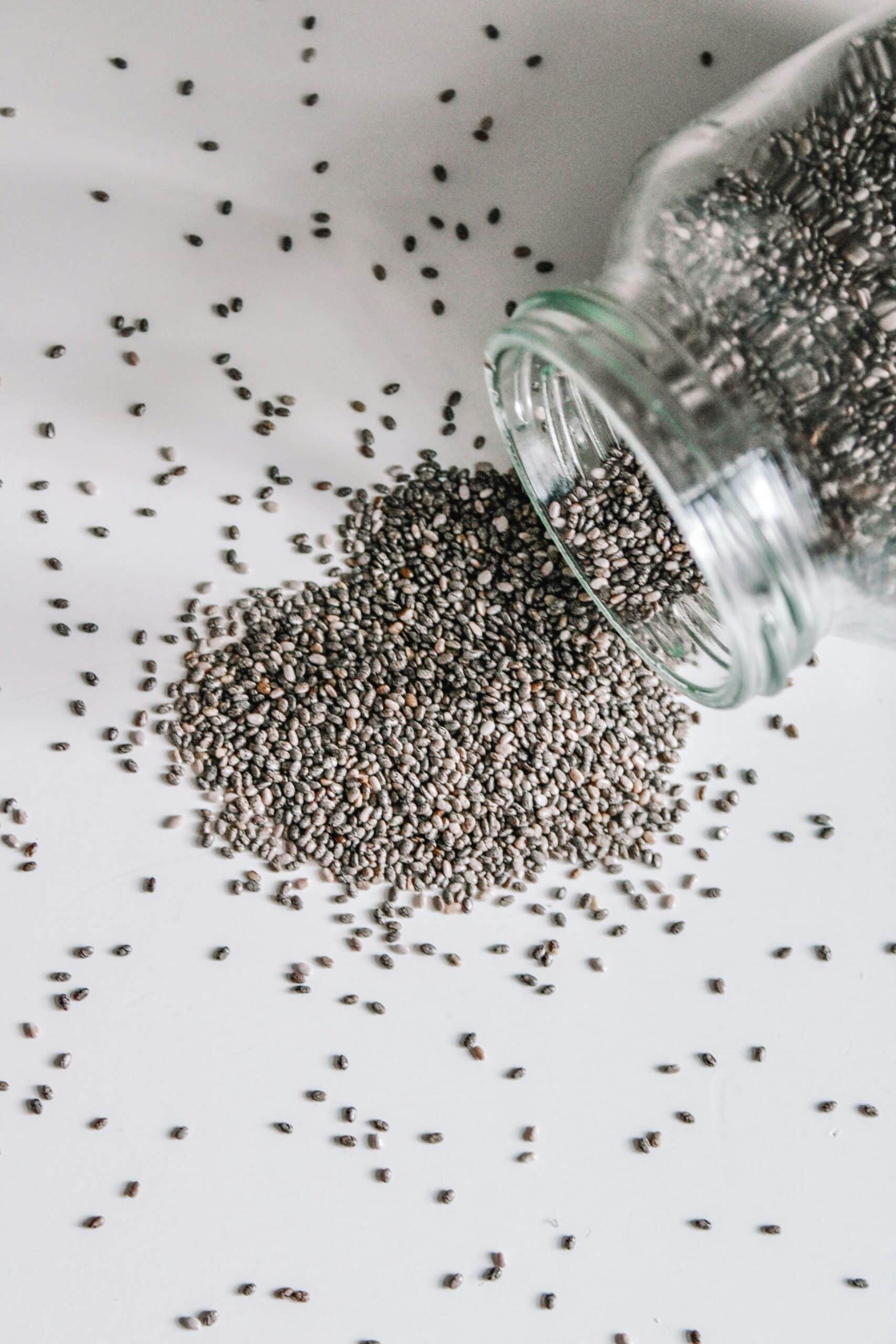 A glass jar spills chia seeds onto a white surface, showcasing a plant-based source of omega-3s for endometriosis support. - Rachael Haverland Site A glass jar spills chia seeds onto a white surface, showcasing a plant-based source of omega-3s for endometriosis support.