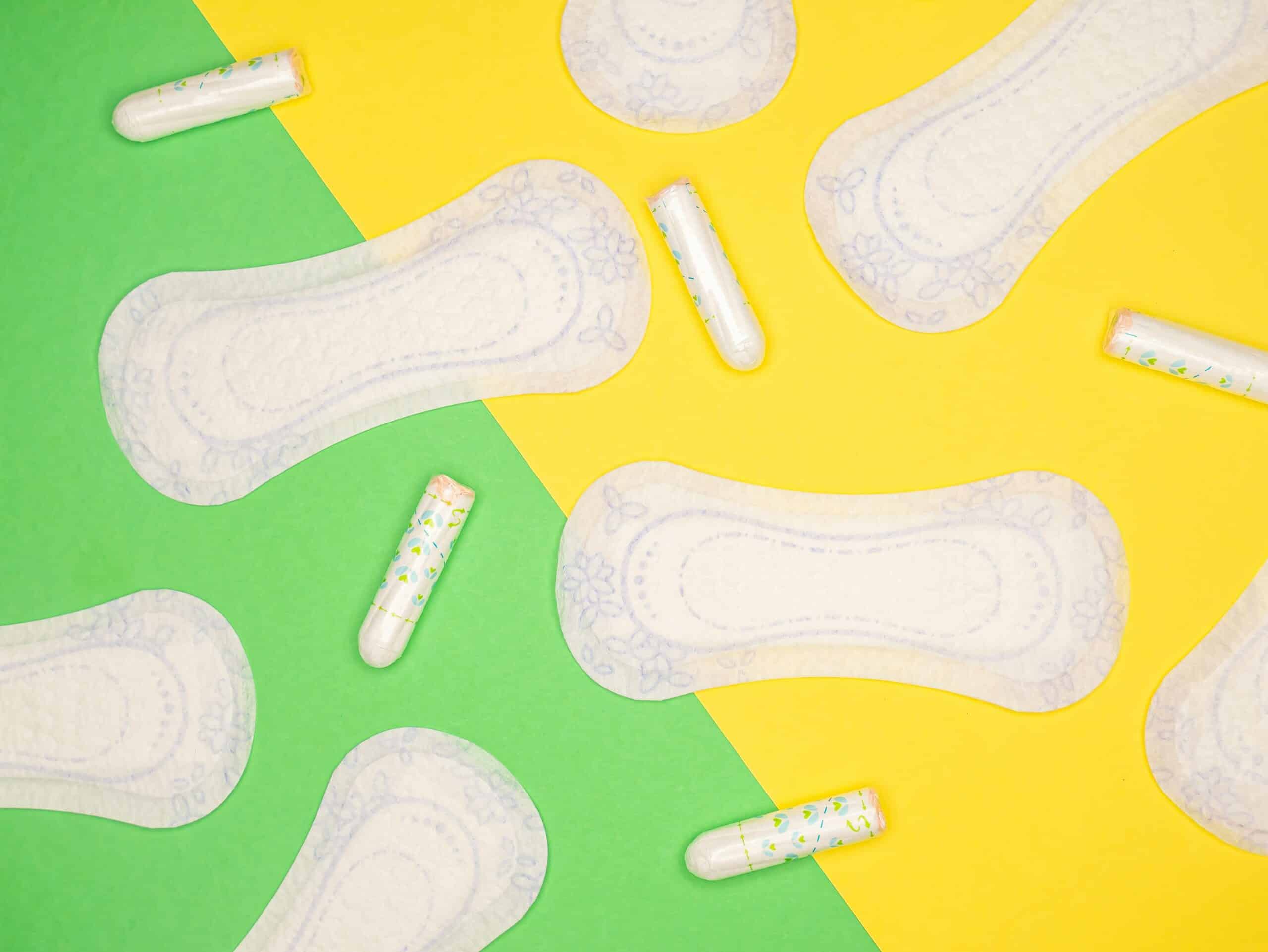 Flat lay of menstrual pads and tampons on a split yellow and green background, representing the menstrual cycle phases affected by endometriosis. - Rachael Haverland Site Flat lay of menstrual pads and tampons on a split yellow and green background, representing the menstrual cycle phases affected by endometriosis.