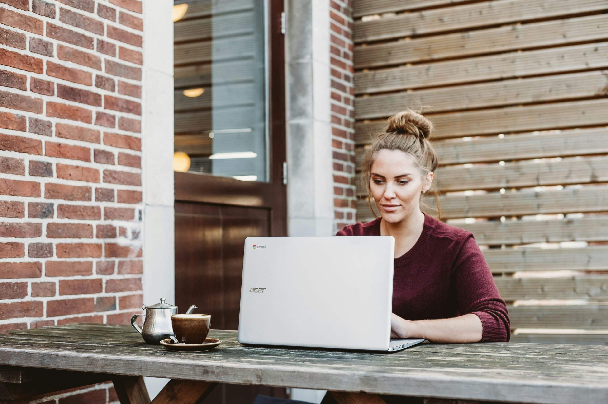 A woman using a laptop at an outdoor table, symbolizing access to online resources and educational tools through endometriosis peer support networks.