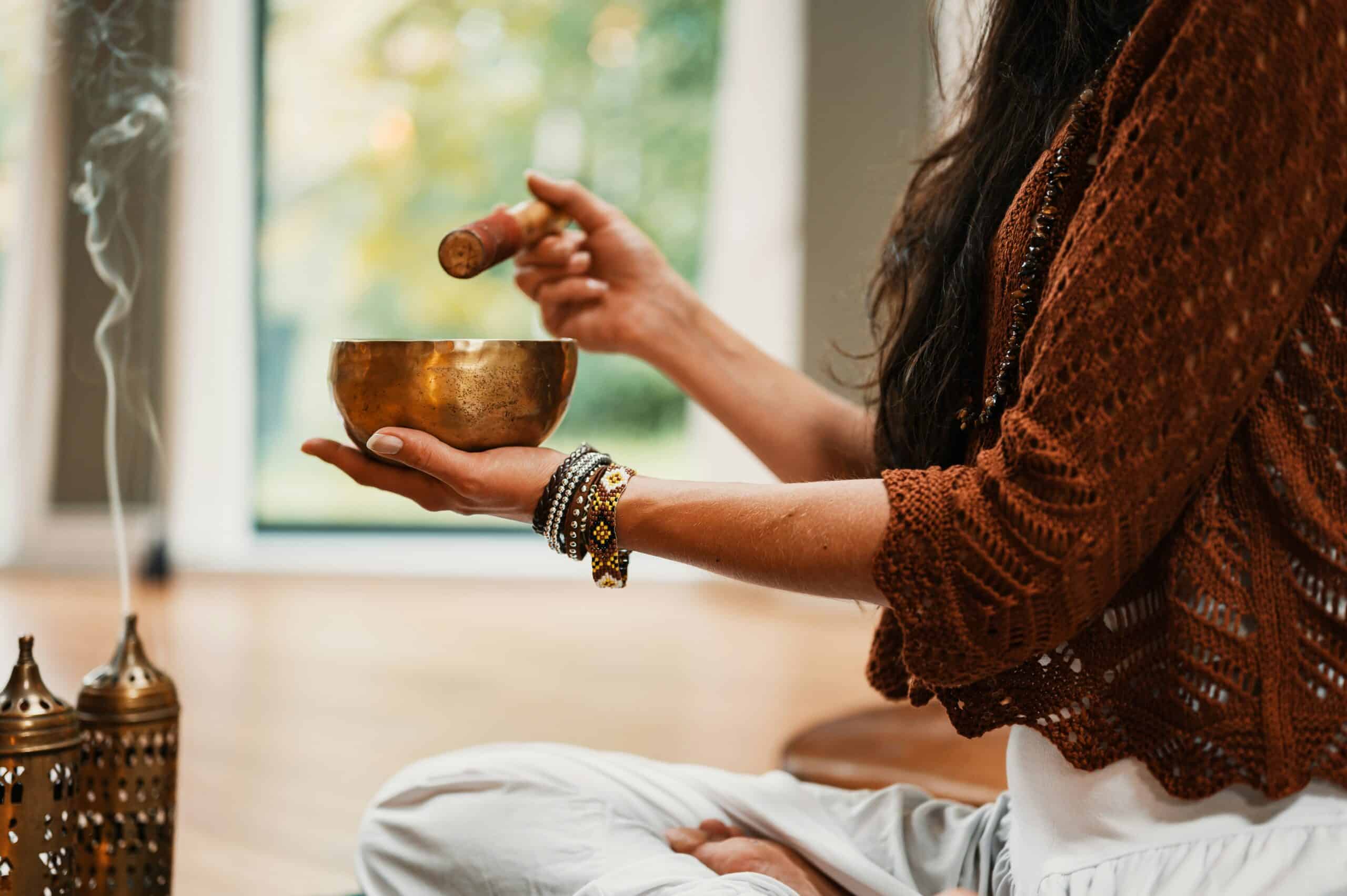A woman practices sound healing with a Tibetan singing bowl and incense, symbolizing holistic stress relief and emotional balance for endometriosis management.