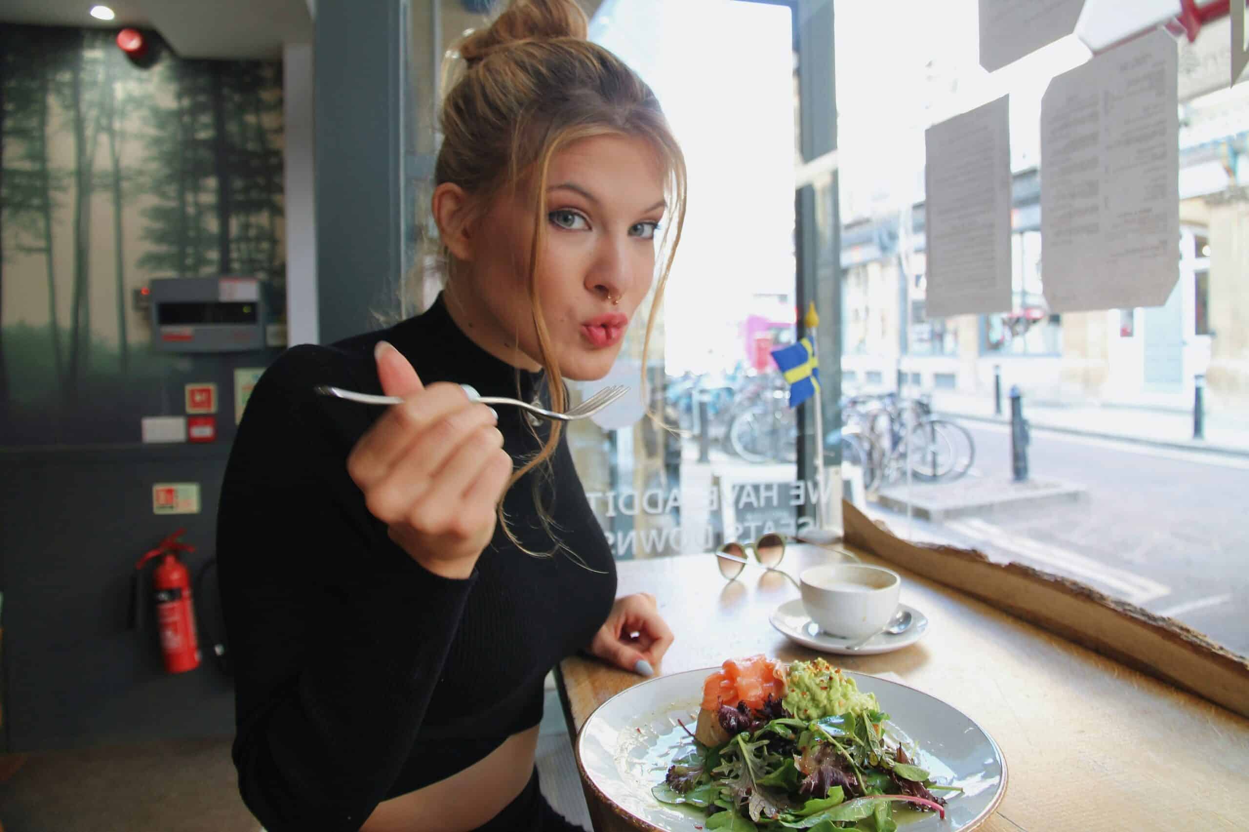 A woman enjoying a healthy meal with leafy greens, salmon, and avocado, highlighting how anti-inflammatory foods can support endometriosis symptom relief. - Rachael Haverland Site Woman enjoying a healthy salad and salmon dish in a café, emphasizing nutritious food choices for managing endometriosis symptoms.