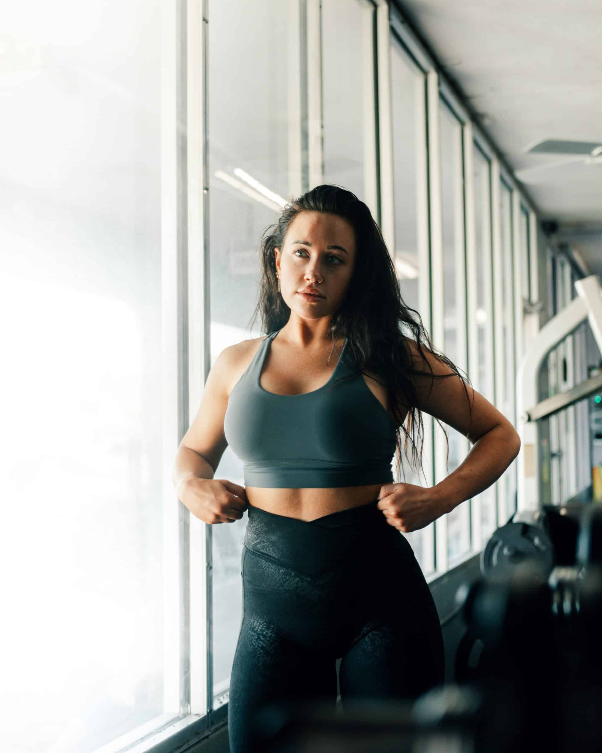 Woman in athletic wear standing confidently in a gym, representing how regular exercise can help manage bloating and endometriosis symptoms. - Rachael Haverland Site Woman in athletic wear standing confidently in a gym, representing how regular exercise can help manage bloating and endometriosis symptoms.