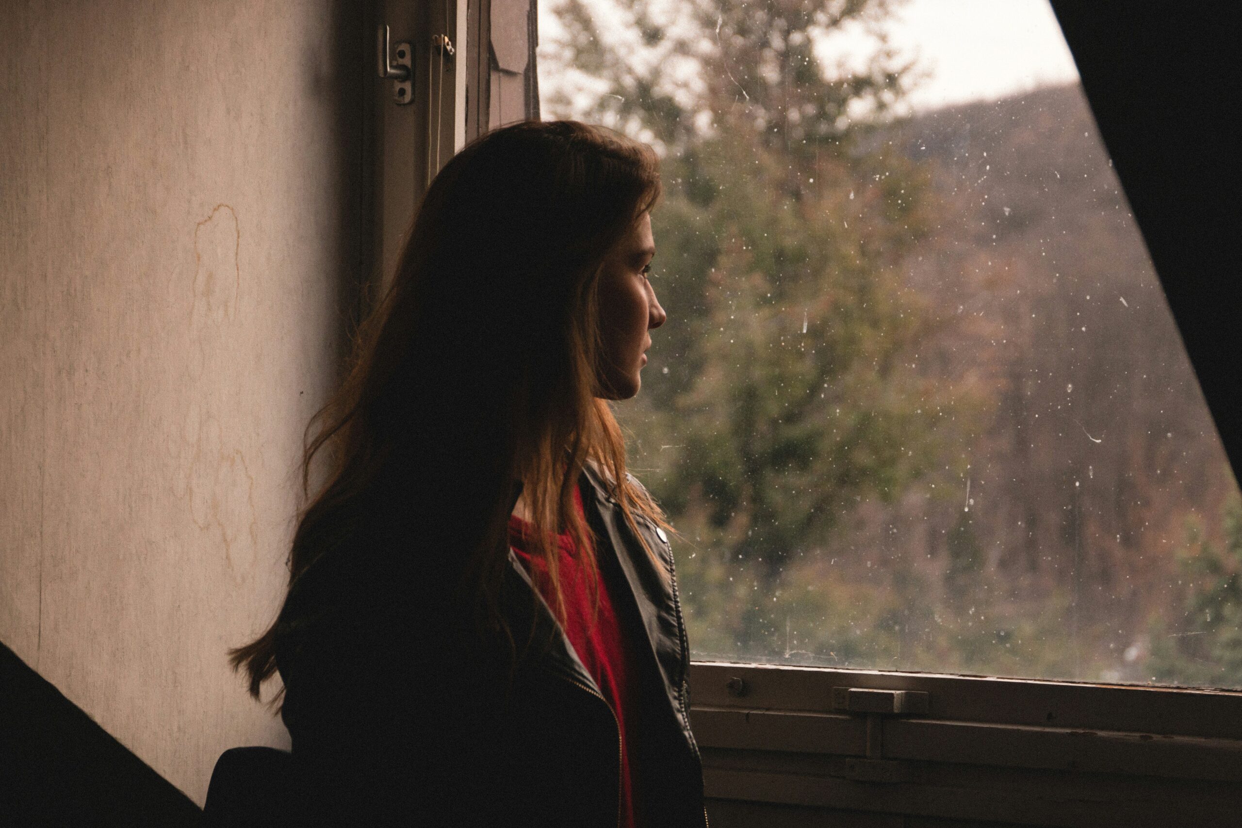 a woman looking out the window - Rachael Haverland Site Woman looking out a window with a contemplative expression, reflecting on personal health and well-being, in the context of managing endometriosis symptoms during menopause.