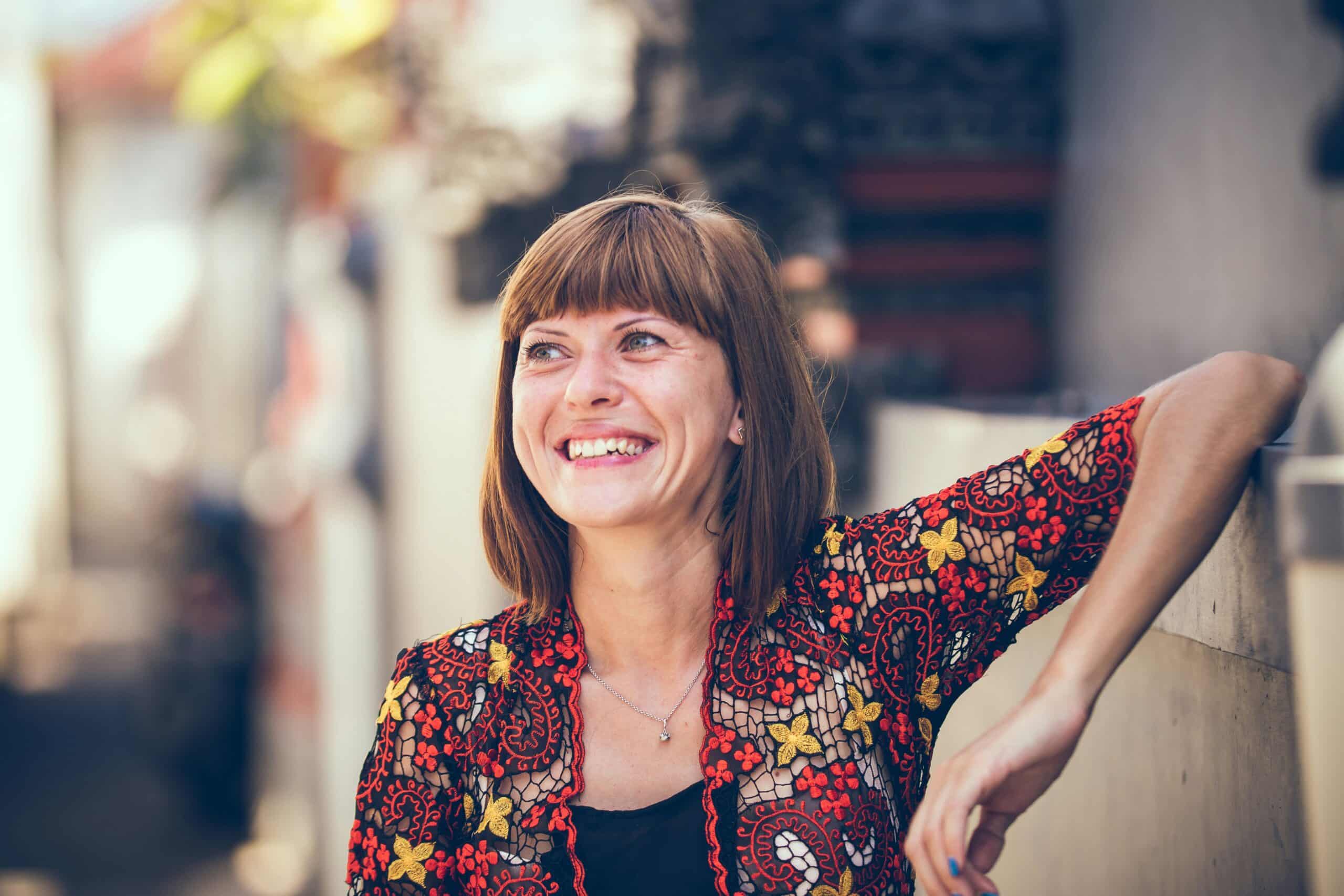 Smiling woman in colorful floral attire, seated casually against a wall, reflecting a positive and relaxed demeanor.
