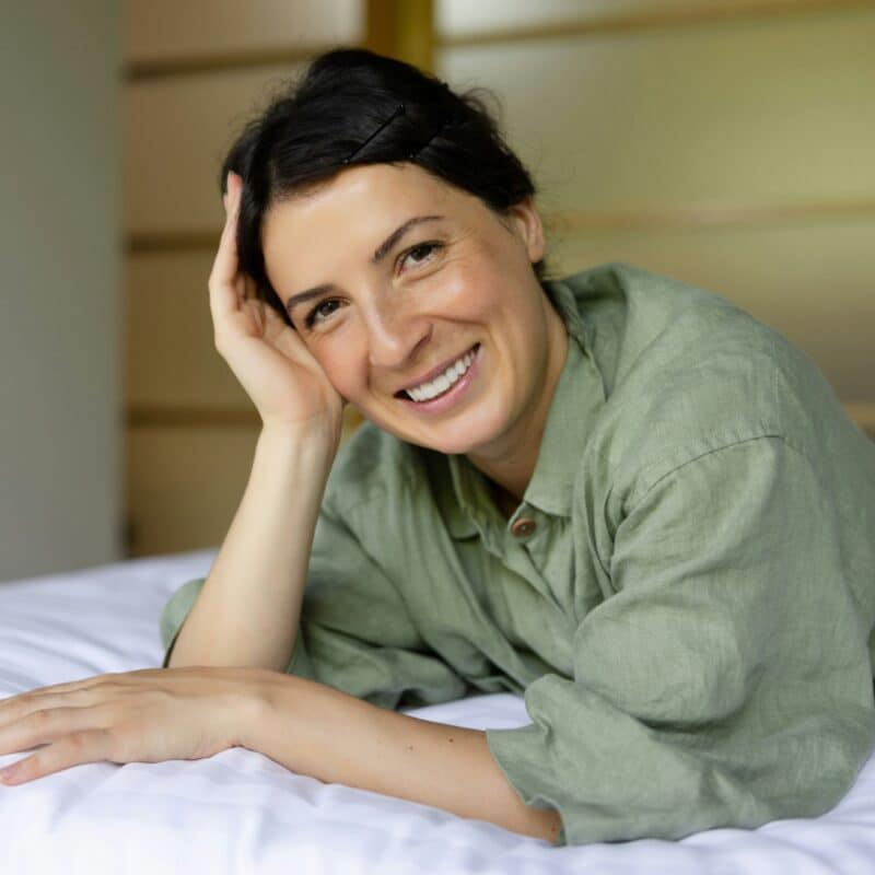 a woman smiling and resting on bed