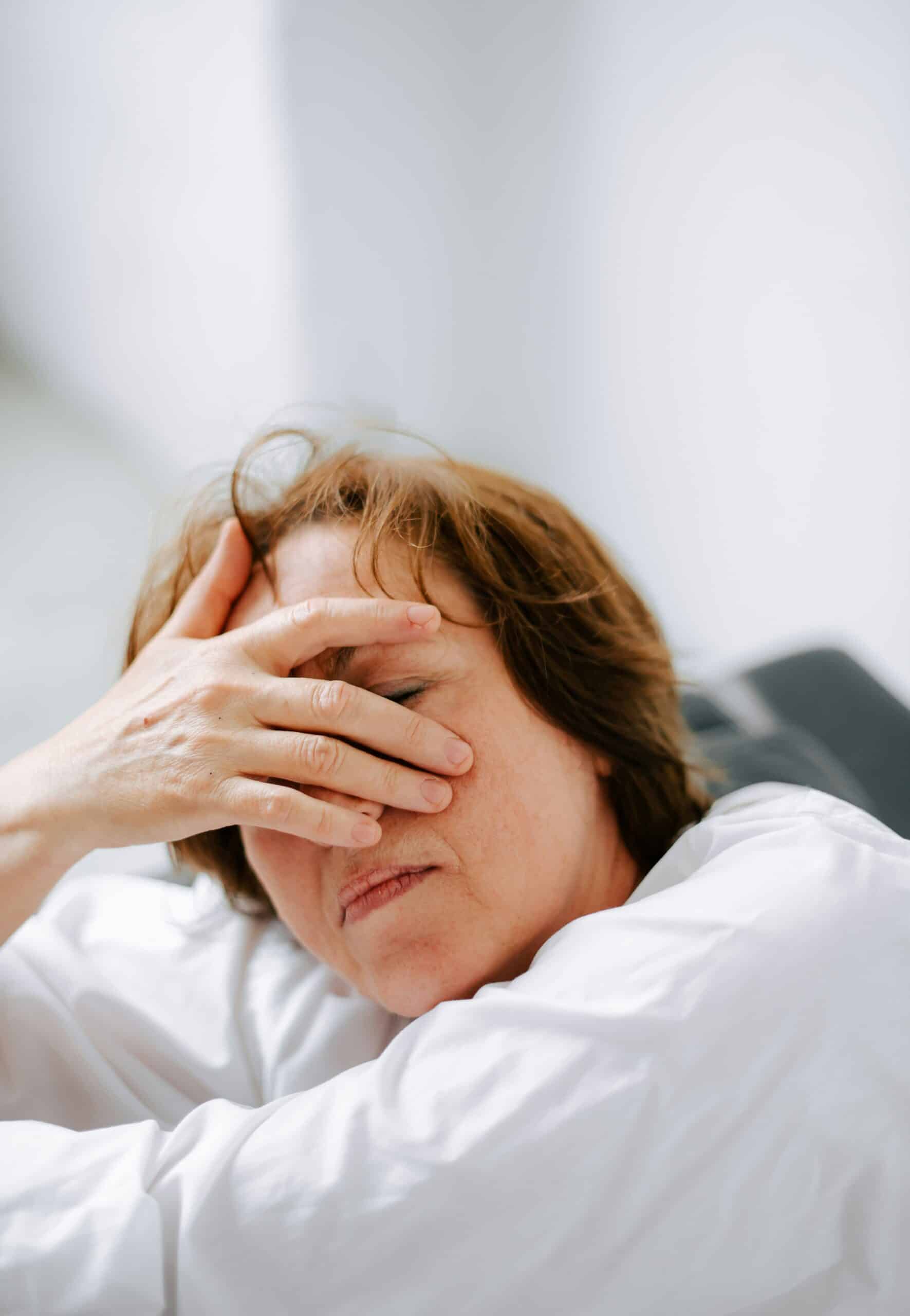a woman stressed out - Rachael Haverland Site Woman with short brown hair expressing discomfort, covering her face with her hand, illustrating the emotional and physical challenges of managing endometriosis during menopause.