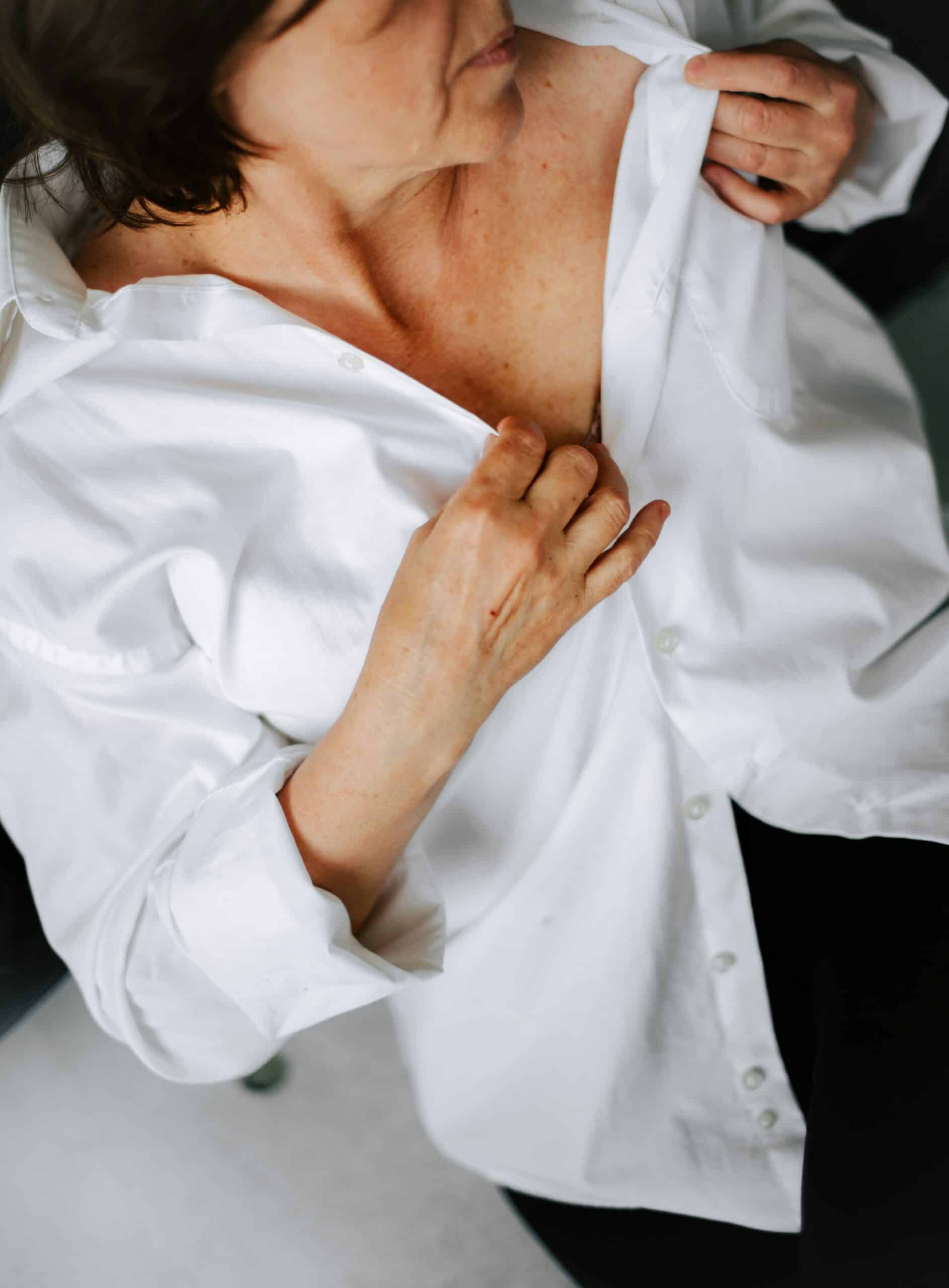 Woman in a white shirt examining her chest, symbolizing self-assessment for health concerns related to endometriosis and menopause.