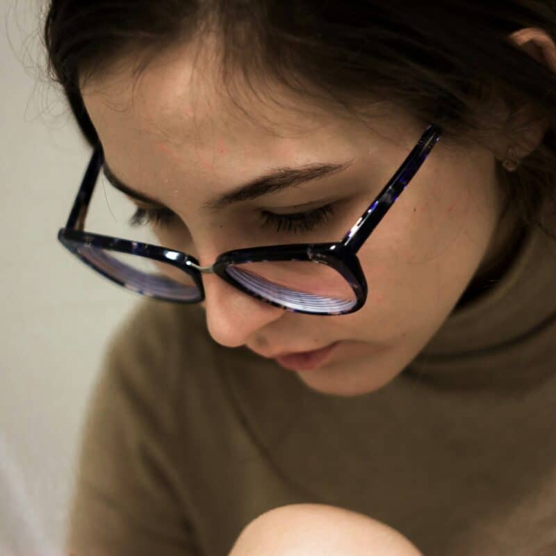 Young woman wearing glasses, focused on reading or writing, in a cozy setting, relevant to endometriosis care and physical therapy discussions.