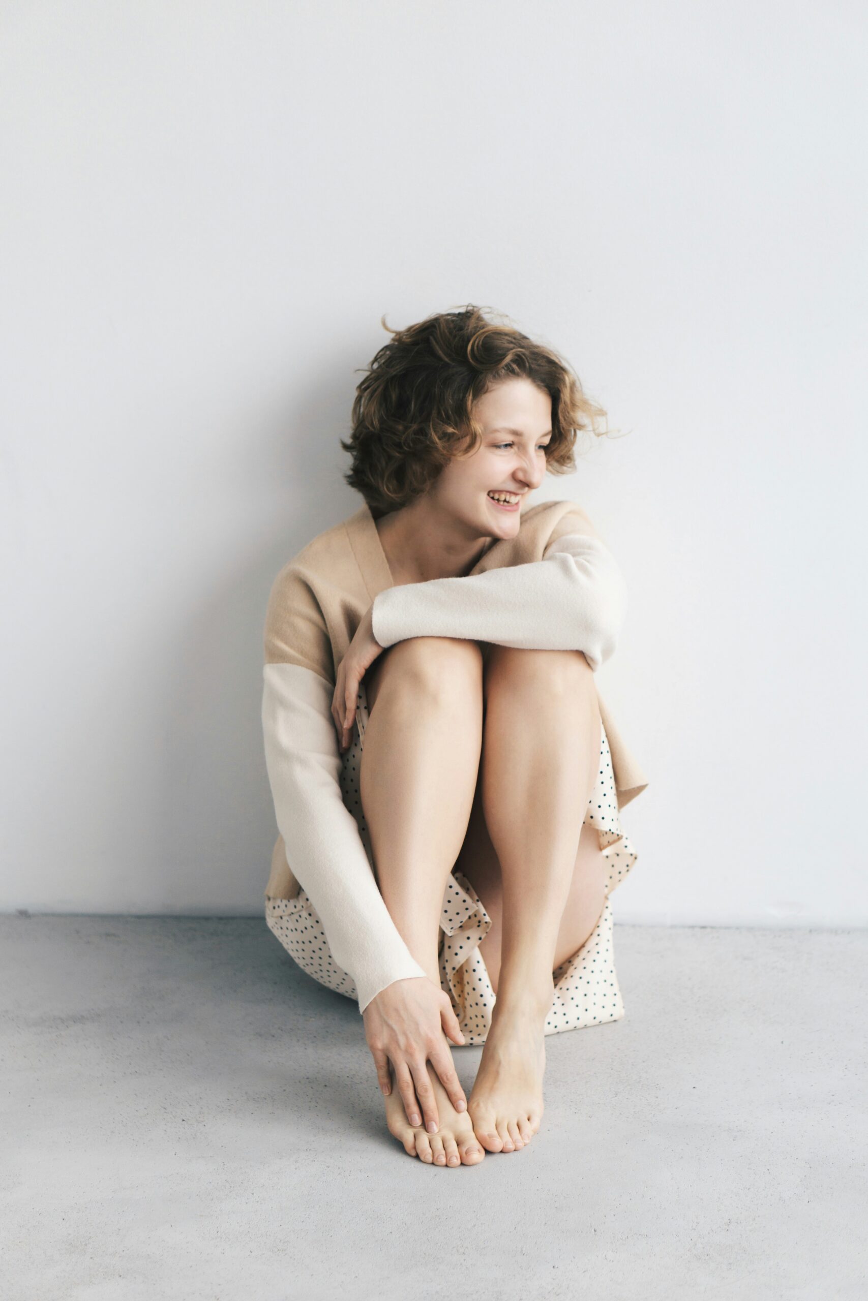Woman seated on the floor, smiling and touching her feet, embodying relaxation and comfort, relevant to manual therapy's role in enhancing mobility and reducing pain for individuals with endometriosis.