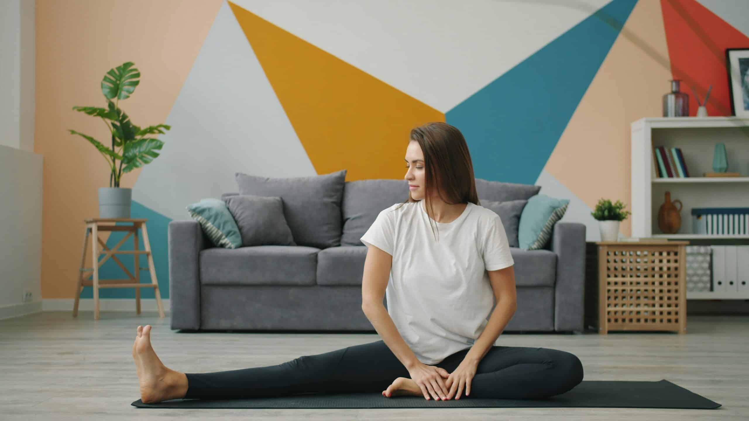 Woman practicing a seated stretch on a yoga mat in a modern living room, emphasizing physical therapy techniques for managing endometriosis pain and improving flexibility.