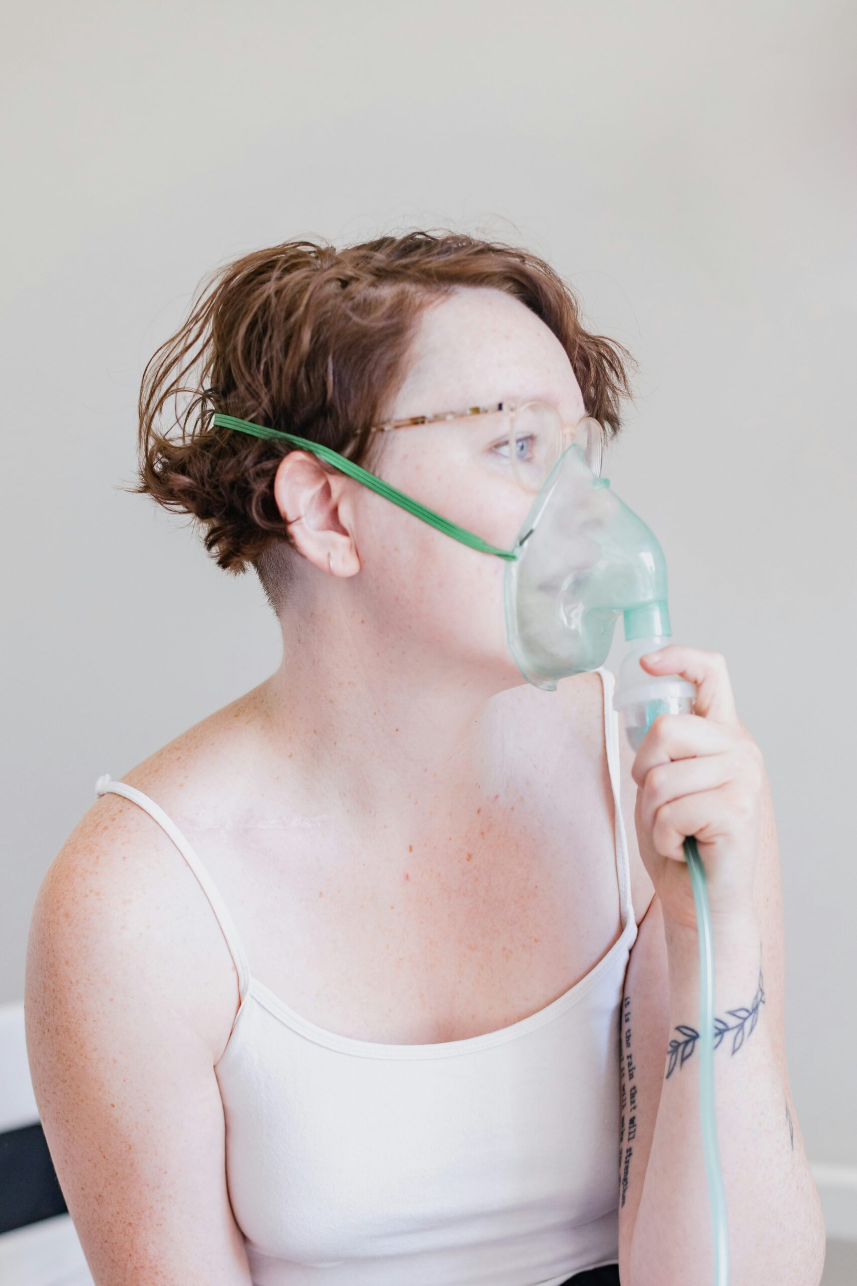 photo 1645273474454 f200e9236fdfjpeg - Rachael Haverland Site Person wearing a medical oxygen mask with a green elastic strap, holding the tubing to breathe.